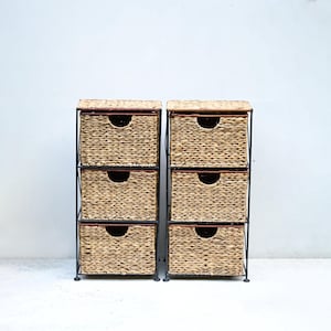 Op de afbeelding: Twee sets van opbergeenheden met drie lades. Elke eenheid heeft geweven, lichtbruine lades met een donkerbruine rand en een zwart metalen frame. De lades hebben een gebogen handgreepopening. De eenheden staan tegen een witte achtergrond.