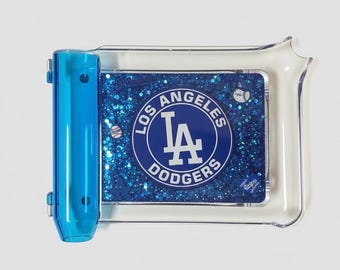 May include: A rectangular clear plastic tray featuring a blue glitter insert with the Los Angeles Dodgers logo in the center. The tray includes a translucent blue cylindrical side attachment and small baseball graphics printed on the glittery surface.