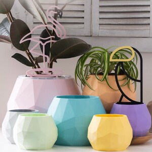 May include: Five geometric planters in different colours and sizes. The planters are made of a textured material and have a modern design. The planters are arranged on a white surface.