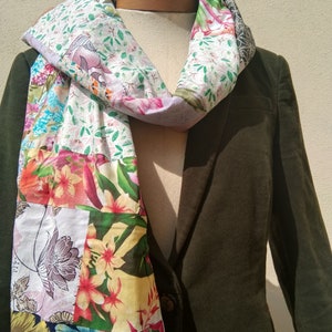 May include: A patchwork scarf with a floral design in shades of pink, blue, and yellow, is draped over a dark green blazer. The scarf is constructed from multiple fabric squares sewn together.