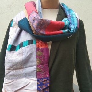 May include: A patchwork scarf made from different fabrics in shades of pink, blue, green, purple, and brown. The scarf is tied around a mannequin's neck.