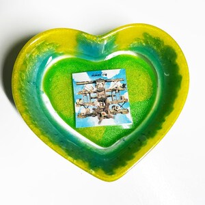 May include: A heart-shaped resin dish with a green and yellow swirl design. The dish has a clear centre with a sticker of a vintage aeroplane.