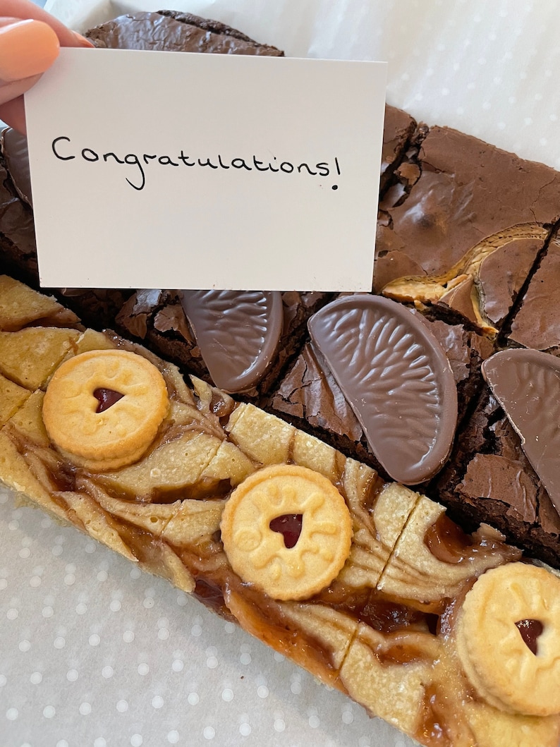 May include: A brownie platter with a card that says "Congratulations!" The platter includes a variety of brownies, including some with orange slices and some with jam and biscuits.