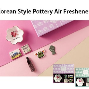 May include: A set of two Korean style pottery air fresheners in purple and green boxes. Each box contains a small white ceramic dish with a floral design, a small ceramic tile with a Korean building design, a small ceramic tile with Korean text, a small ceramic tile with a traditional Korean clothing design, and a small bottle of essential oil.
