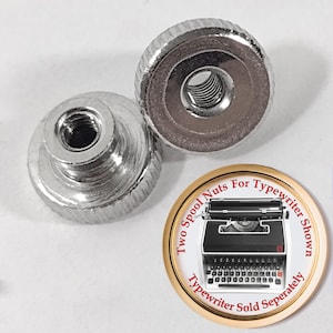 May include: Two silver spool nuts for a typewriter. The nuts have a ridged edge and a threaded center. A circular graphic shows a typewriter and text that reads "Two Spool Nuts For Typewriter Shown, Typewriter Sold Separately."