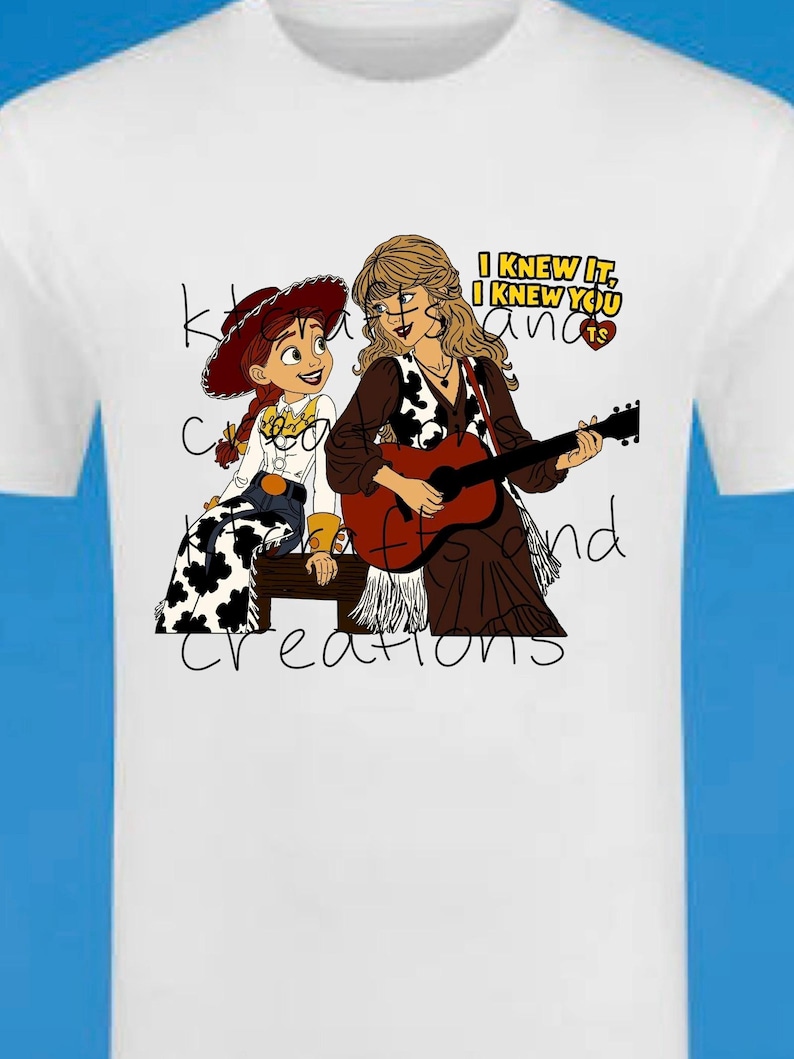 May include: A white t-shirt featuring a graphic illustration of a cowgirl character with red hair and a blonde woman playing an acoustic guitar. The text "I KNEW IT, I KNEW YOU" is printed in yellow and black, with a small red heart containing the letters TS.
