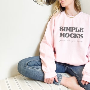 May include: A pink sweatshirt with the text "SIMPLE MOCKS your design here" in black. The sweatshirt is being worn by a person sitting on a striped surface.