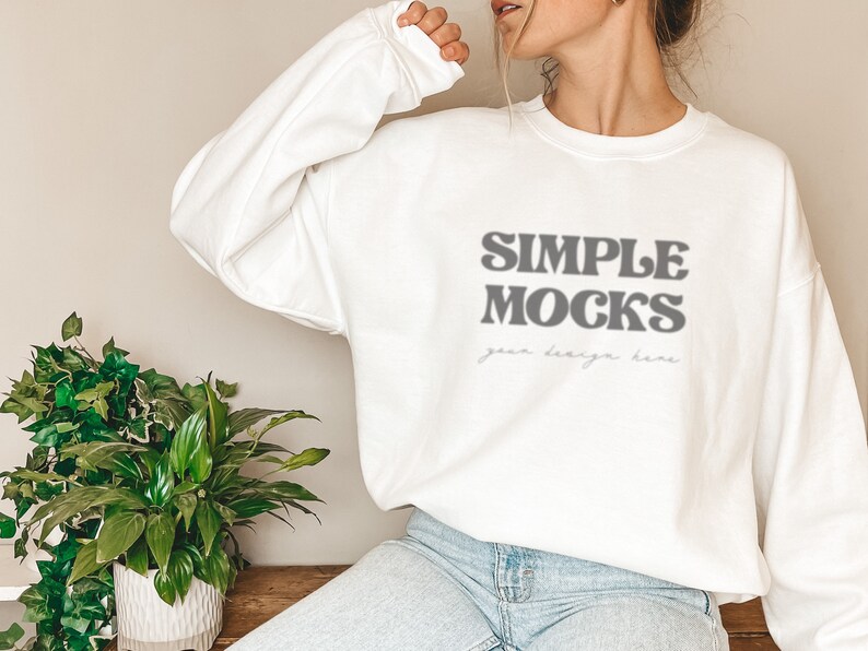 May include: White long-sleeved sweatshirt with the text "SIMPLE MOCKS" in a retro font. The text "your design here" is written in a smaller font below the main text.