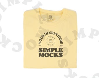 May include: A yellow t-shirt with a brown circle design that says "Your Design Here" with a smaller circle inside that says "100% Real People" and "Est'd 2021" below the circle. The text "Simple Mocks" is below the circle.