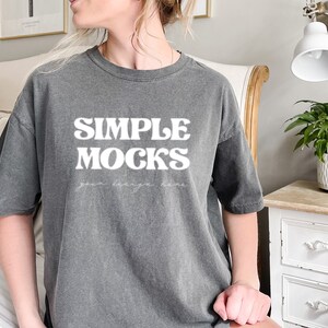 Può includere: Una maglietta oversize grigio antracite con il testo "SIMPLE MOCKS" in bianco. Il testo è in uno stile di font retrò.