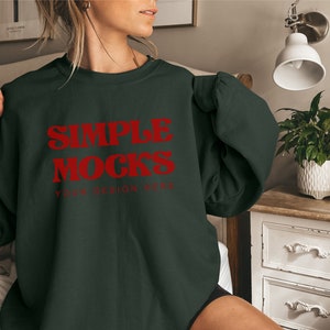 Op de afbeelding: Een donkergroen sweatshirt met de tekst "SIMPLE MOCKS YOUR DESIGN HERE" in rode letters.