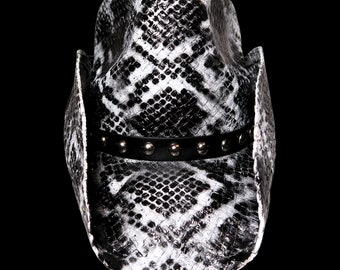Pode incluir: Um chapéu de cowboy com padrão de pele de cobra em preto e branco. O chapéu tem uma faixa preta com tachas prateadas. Um acessório de moda em estilo western.