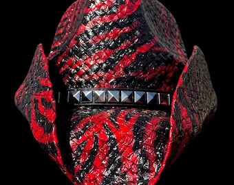 Può includere: Un cappello da cowboy rosso e nero con un design in paglia intrecciata. Il cappello presenta una fascia borchiata intorno alla corona. Il cappello ha un'ampia tesa e una classica forma da cowboy.
