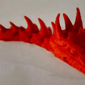 May include: A bright red 3D printed dragon figurine with a long, segmented body and a detailed head with sharp teeth and horns.