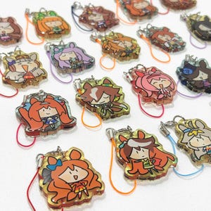 以下が含まれることがあります： アニメスタイルのキャラクターデザインが施された、カラフルなアクリルチャームのコレクション。各チャームには、さまざまな髪の色と衣装を持つユニークなキャラクターがおり、カラフルなストラップが付いたシルバーカラーの留め金が付いています。