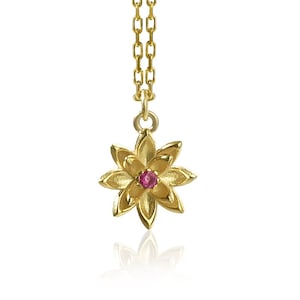 May include: A gold necklace with a delicate flower pendant featuring a small pink gemstone in the center.