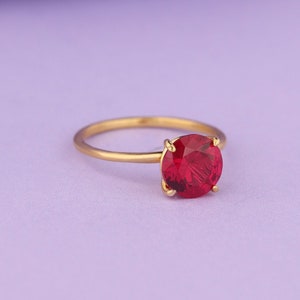 May include: A gold ring with a large, round, red gemstone.