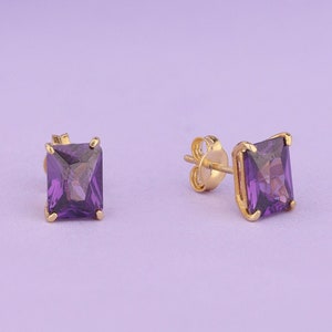 May include: A pair of gold earrings with square-shaped purple gemstones.