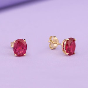 May include: A pair of gold stud earrings with oval-shaped red gemstones.