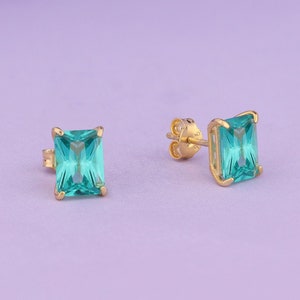 May include: A pair of gold earrings with square-shaped turquoise blue gemstones.