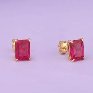 May include: A pair of gold earrings with red square-shaped gemstones.