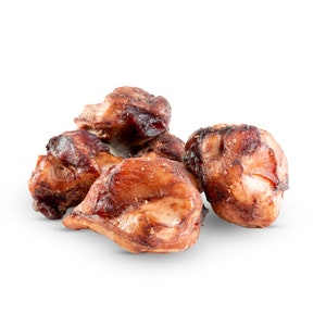 May include: A pile of cooked, brown dog treats with a slightly charred appearance. The treats have a textured surface and are arranged on a white background. The image highlights the natural, meaty look of the dog chews.
