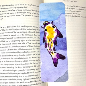 May include: A watercolour illustration of a purple and yellow fish with a halo. The fish is swimming in a blue and purple watercolour background.