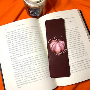 Peut inclure: Un marque-page brun avec une illustration aquarelle d'une citrouille. Le marque-page porte le texte "Hello Pumpkin".