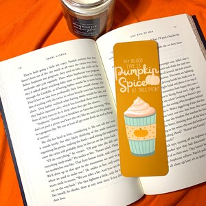 May include: A gold bookmark featuring a pumpkin spice latte illustration and the text "My blood type is pumpkin spice at this point".
