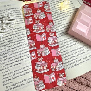 Peut inclure: Un marque-page rouge avec un motif de livres roses et rouges, de cœurs et de bougies. Le marque-page est conçu pour ressembler à une pile de livres.