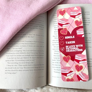 Puede incluir: Un marcapáginas rosa y rojo con un patrón de cuadros rosa y blanco. El marcapáginas presenta un corazón con un patrón de lunares rosa y blanco y el texto "Soltero, En pareja, Enamorado de personajes ficticios".