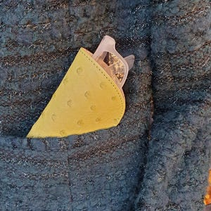 May include: A yellow, textured, semi-circular glasses case with visible stitching along the curved edge, containing a pair of light-colored eyeglasses, tucked into the pocket of a dark teal, chunky, metallic-flecked knit jacket.
