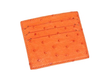 Könnte beinhalten: Ein leuchtend orangefarbener Kartenhalter mit einer strukturierten Oberfläche und ausgeprägten Federfollikelmustern. Das rechteckige Accessoire verfügt über drei horizontale Schlitze zur Kartenaufbewahrung sowie sichtbare Nähte an den Kanten.