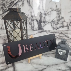 May include: Black metal sign with a pink horseshoe and the word "BEAUTY" in pink lettering.