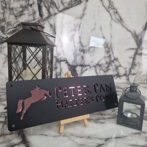 May include: Black metal sign with a rose gold horse silhouette and the text "PETER PAN HARPER'S PONY".