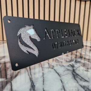 May include: Black metal sign with a silver glitter horse silhouette and the text "APPLEJACK 07303 833962".