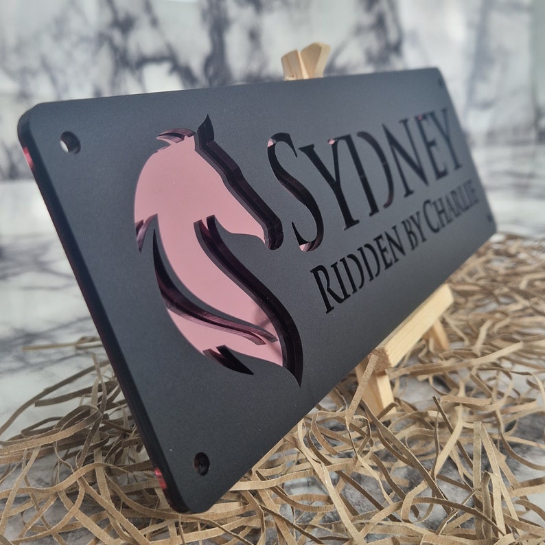 May include: Black acrylic horse stall sign with a pink horse silhouette and the text "Sydney ridden by Charlie".