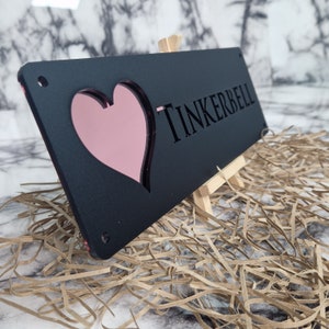 May include: Black wooden sign with a pink heart cutout and the name "TINKERBELL" engraved in white.