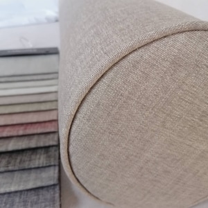 May include: A beige cylindrical pillow with a textured fabric cover. The pillow is made of a soft, comfortable material and is perfect for adding a touch of style to any room.