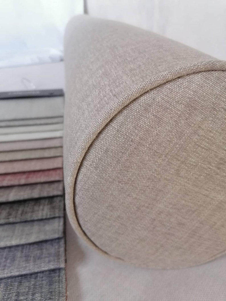 May include: A beige cylindrical pillow with a textured fabric cover. The pillow is made of a soft, comfortable material and is perfect for adding a touch of style to any room.