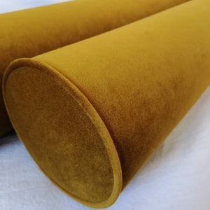 Può includere: Due cuscini cilindrici di colore giallo senape in tessuto di velluto morbido.