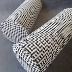 Może przedstawiać: Dwa cylindryczne poduszki w czarno-biały wz&oacute;r w kratę. Poduszki są wykonane z miękkiej, tkanej tkaniny.