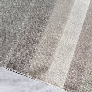 May include: A close-up of a fabric swatch with a gradient of beige, brown, and gray colors. The fabric has a textured, woven appearance.