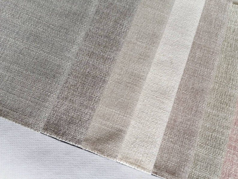May include: A close-up of a fabric swatch with a gradient of beige, brown, and gray colors. The fabric has a textured, woven appearance.