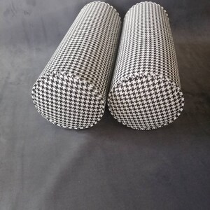 Może przedstawiać: Dwa cylindryczne poduszki w czarno-biały wz&oacute;r w kratę. Poduszki są wykonane z miękkiej, tkanej tkaniny.