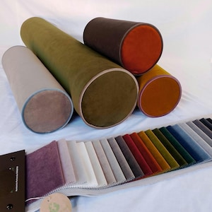 May include: Four cylindrical pillows in various shades of green, brown, and orange with contrasting trim. A fabric swatch book with a variety of colors is displayed below the pillows.