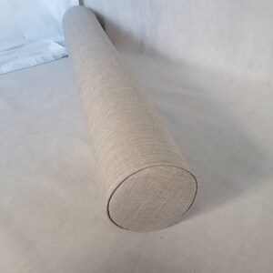 May include: A beige cylindrical pillow with a textured fabric cover.