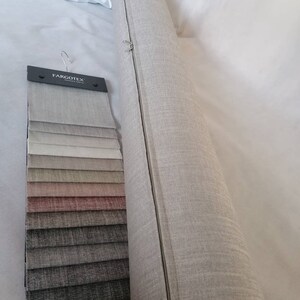 May include: A roll of beige fabric with a zipper running down the side. A fabric swatch book with a variety of colors and textures is next to the roll. The swatch book has the text "Fargotex" on the front.