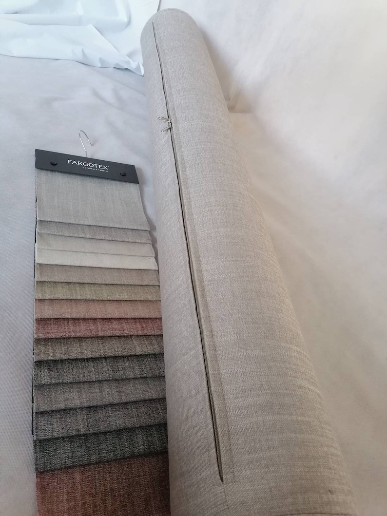 May include: A roll of beige fabric with a zipper running down the side. A fabric swatch book with a variety of colors and textures is next to the roll. The swatch book has the text "Fargotex" on the front.
