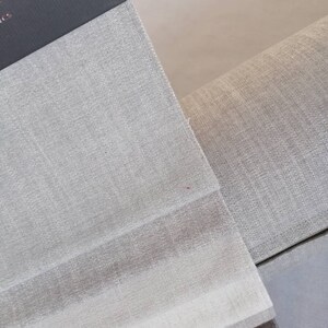 May include: Close-up of a fabric swatch book with different shades of gray linen fabric. The swatches are arranged in a stack, with the lightest shade on top and the darkest shade on the bottom.
